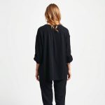Back view of a model wearing the boho clothing brand chai loose leaf top in black, studio shot.