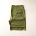 Olive green golf skorts scrunch bum leggings neatly folded on a neutral surface, top-down flat lay view.
