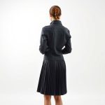 Back view of a model wearing a charcoal pleated golf skirt and golf waterproof jacket, studio shot on white background.