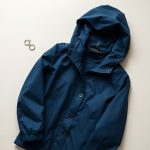 Navy Blue womens anorak jacket waterproof silver earrings folded flat lay on neutral background.
