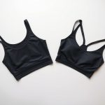 Flat lay of charcoal women's yoga shirts and yoga bras neatly folded on a neutral surface.