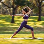 Woman in a purple yoga crop and pants performing a yoga pose in an Australian park.