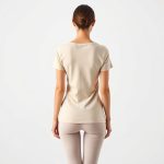 Back view of a beige organic activewear yoga t shirt on a model, studio shot.